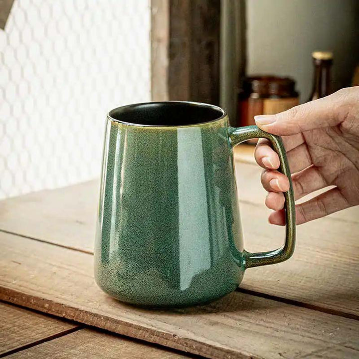 Green ceramic mug held by a hand on a wooden surface