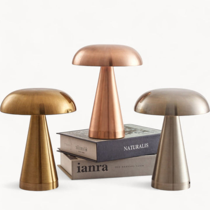 Trio of rechargeable table lamps in brushed gold, copper, and silver finishes on stacked books.