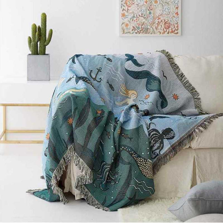 Decorative blanket with mermaid and sea creature pattern draped over a couch, ideal for home decor.