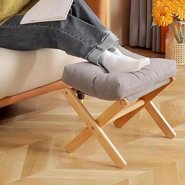 Low footrest with plush grey cushion in front of sofa, used for casual lounging in Scandinavian-style room with wood flooring.