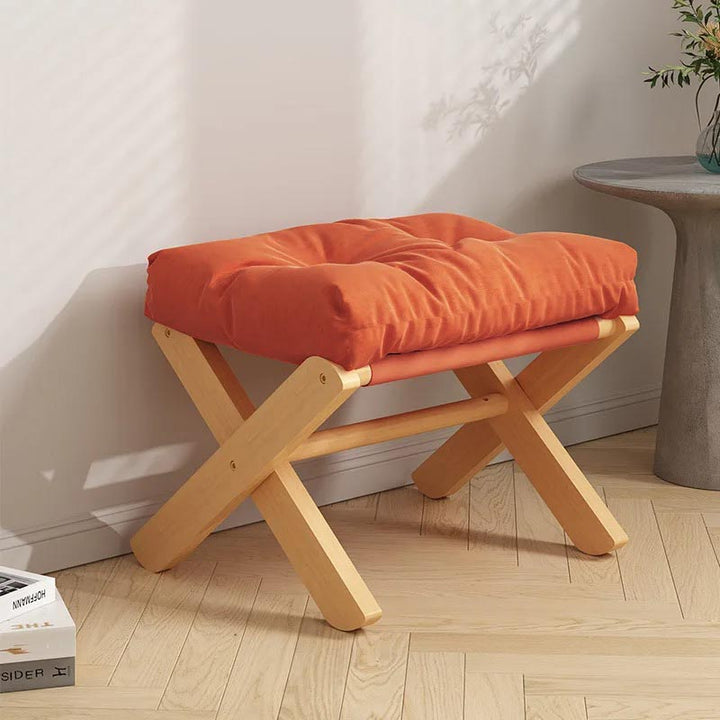 Foldable orange footstool with soft cushion placed near wall, natural wood base ideal for Nordic or Japandi-style UK interiors.