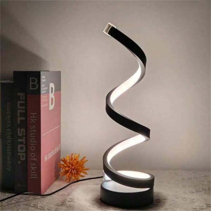 Modern spiral table lamp on a wooden surface with books in the background