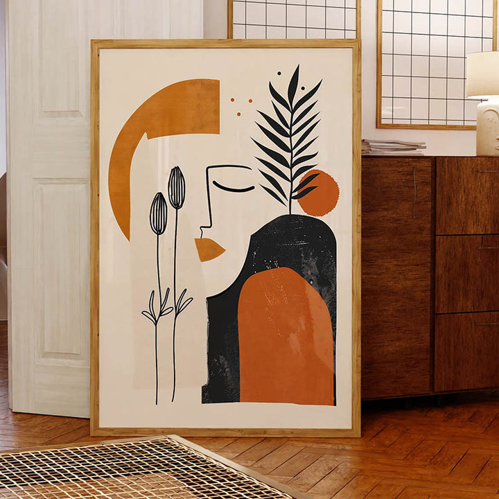 Scandinavian-style abstract canvas print in bold burnt-orange and black tones, featuring a face and foliage, with natural wood frame.