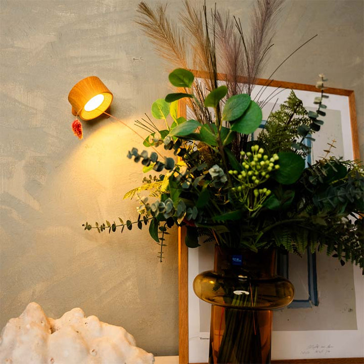 Decorative vase with greenery against a wall with a framed picture and light fixture.