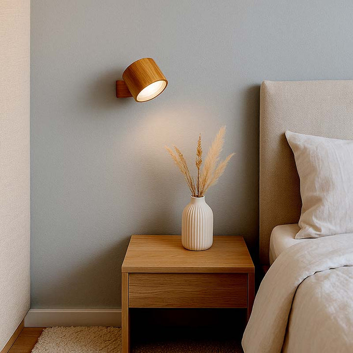 Wooden nightstand with a vase and dried plants next to a bed with beige bedding.