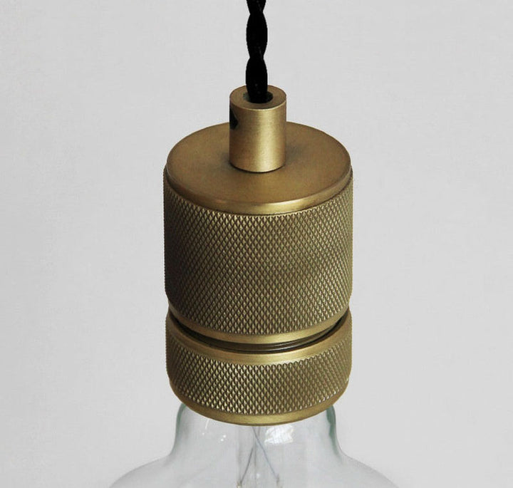Brass textured lampshade on a clear glass base against a light gray background