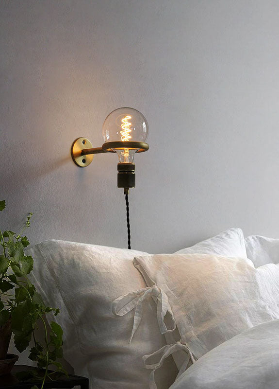 Wall-mounted light fixture with a clear glass shade on a neutral wall above a white sofa.