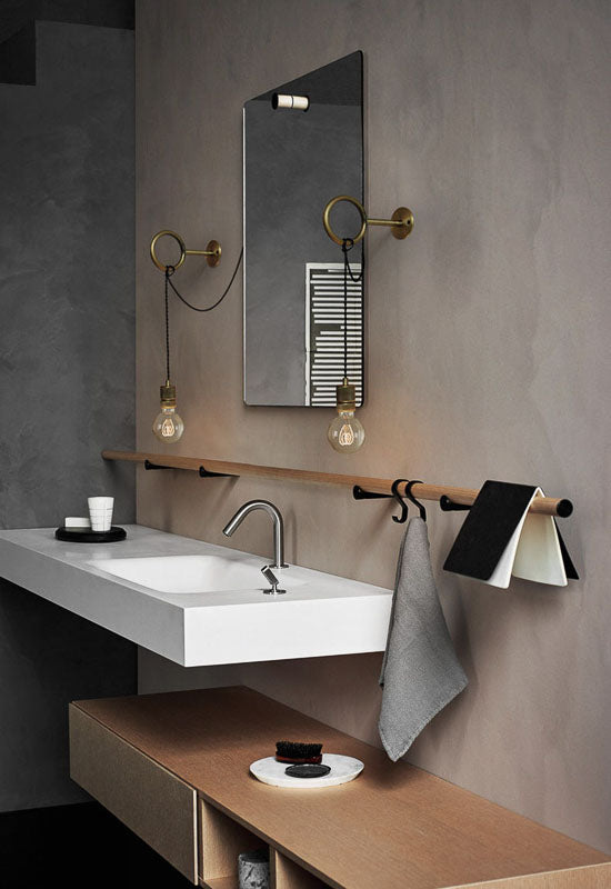 Modern bathroom with a sink, mirror, and towel rack against a gray wall.