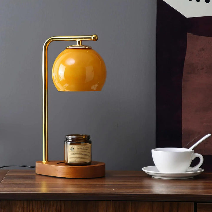 Yellow table lamp on a candle warmer  surface with a cup and saucer and a candle.