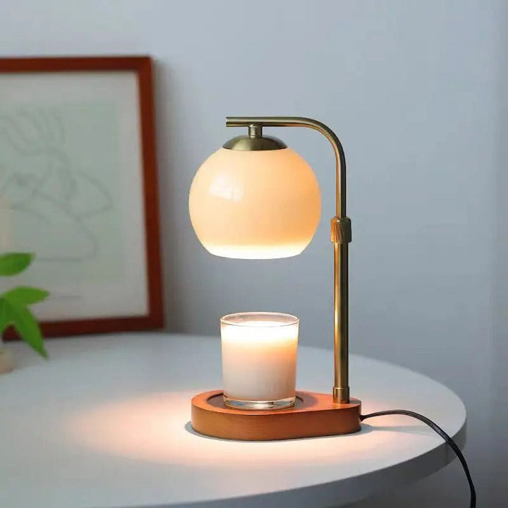 Table lamp with a candle holder on a white surface, with a light blue wall and framed picture in the background.