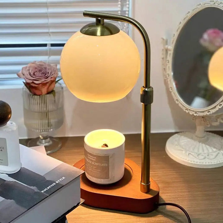 Table lamp with a candle warmer warm glow on a wooden surface next to a candle and a book.