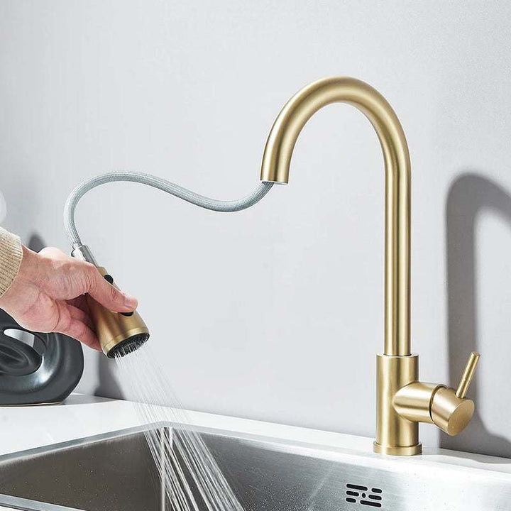 Hand using gold pull-out kitchen faucet sprayer with flexible hose over stainless sink.