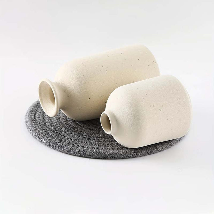 Two beige ceramic vases on a gray woven mat against a white background