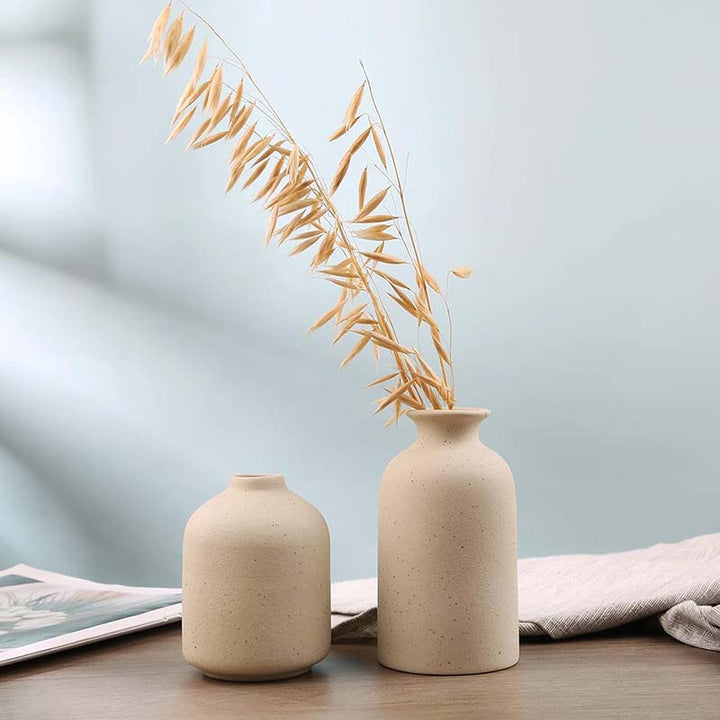 Two beige vases with dried leaves on a light blue background