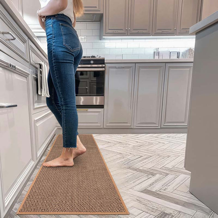 Person wearing blue jeans standing on a brown kitchen mat in a modern uk kitchen.
