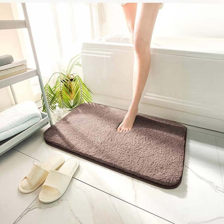 Brown bath mat on a white tiled floor with a person stepping onto it.