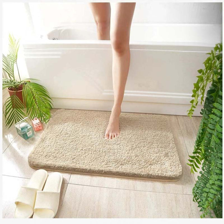 Person stepping onto a beige bath mat in a bathroom setting with plants and a bathtub.