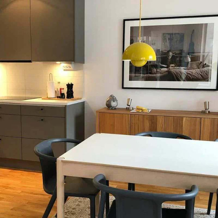 Modern kitchen with a dining table and chairs, featuring a yellow pendant light and framed picture on the wall.