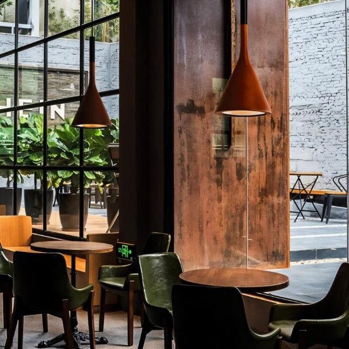 Modern restaurant interior with wooden tables, green chairs, and pendant lights.