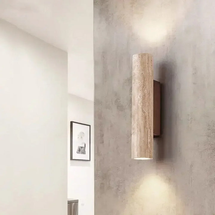 Wall-mounted cylindrical light fixture on a textured wall with a framed picture in the background.