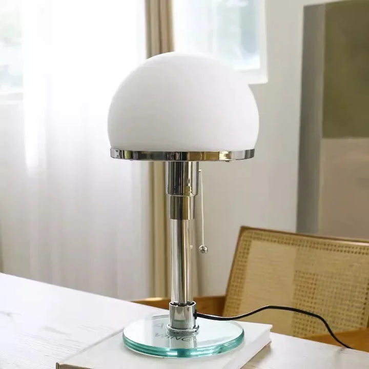 Glass ball Bauhaus bedside lamp with chrome stand on white desk near window