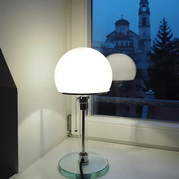 White glass dome Bauhaus table lamp glowing warmly on windowsill