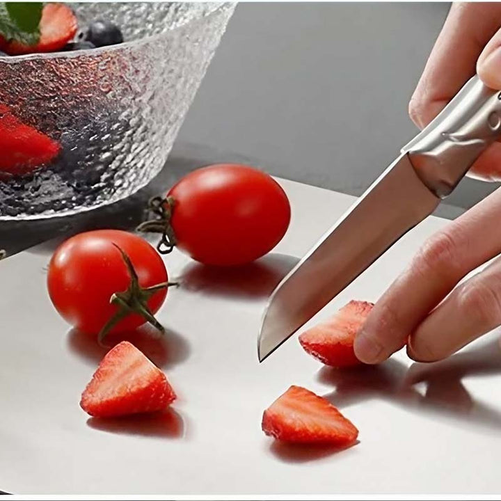 Person slicing strawberries with a knife Stainless-Steel Chopping Board, with tomatoes and a glass bowl in the background.