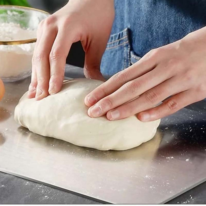 Person kneading dough on a Stainless-Steel Cutting Board with a bowl of flour in the background.