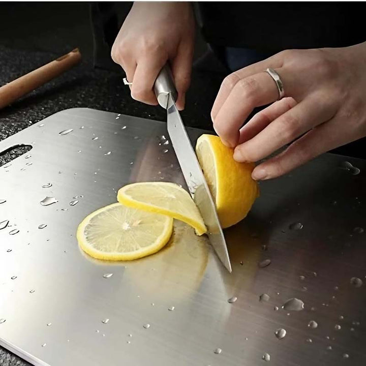 Person slicing a lemon on a Stainless-Steel Chopping Board board with water droplets.