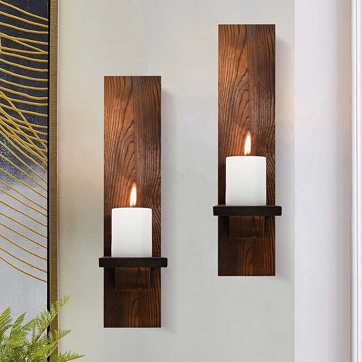 Two wooden wall sconces with candles on a light gray wall.
