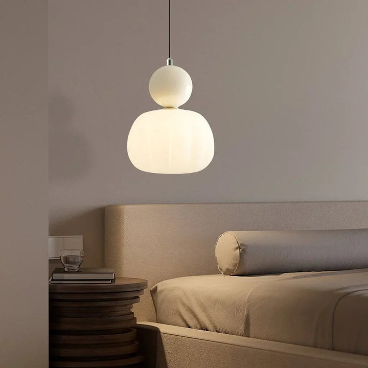 Cream Art Deco pendant lamp with round top accent glowing warmly above nightstand