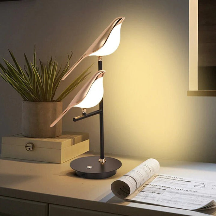 Warm golden bird table lamp lighting up cozy home office desk setup.