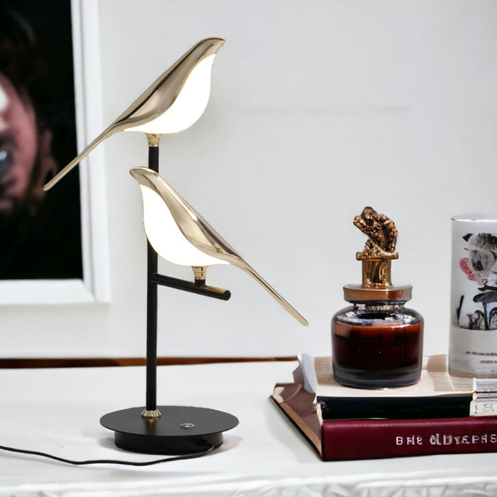 Decorative LED bird lamp on table with framed photo and books in background.
