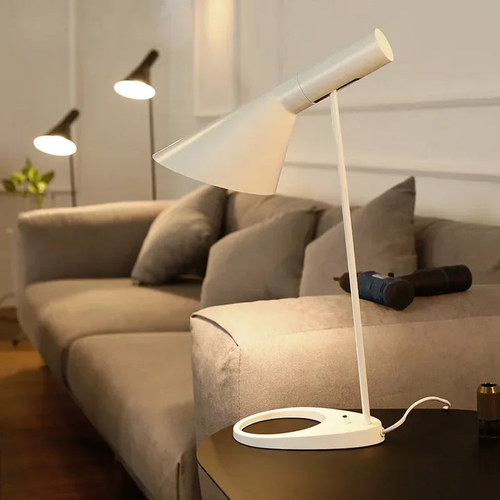 White SPIRE industrial table lamp on black side table beside grey sofa in living room.