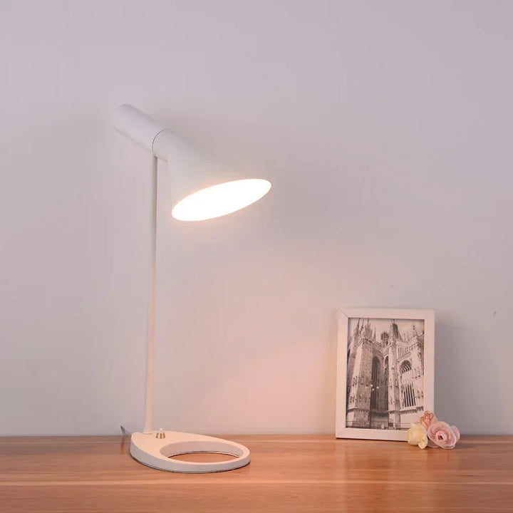White SPIRE bedside table lamp with soft warm light on wooden desk with framed photo.