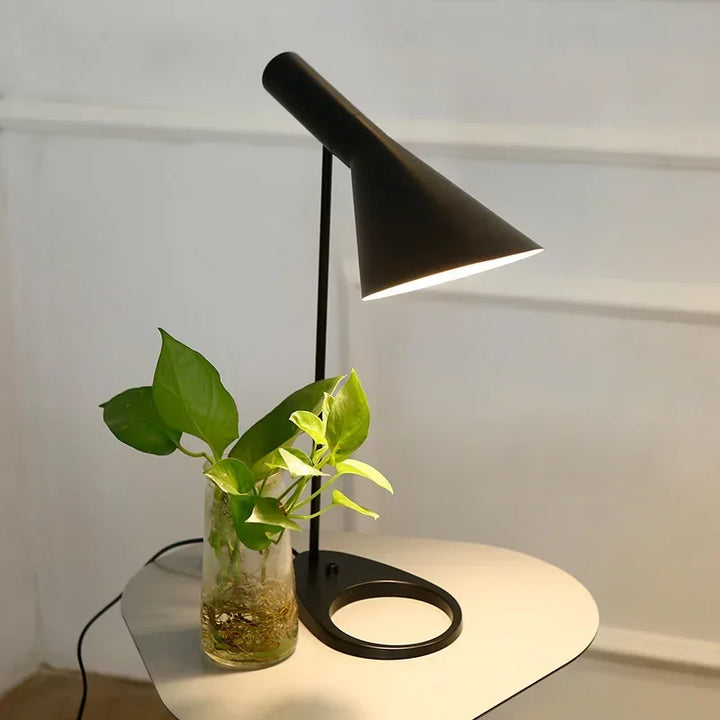 Black SPIRE modern table lamp on white side table beside glass vase with green plant.