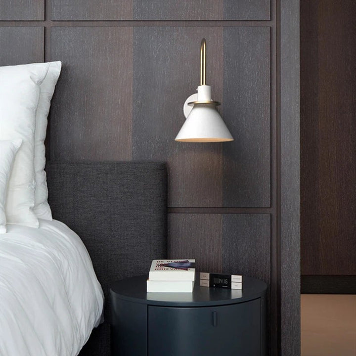 Bedroom with a nightstand, books, and a wall-mounted lamp against a patterned wall.