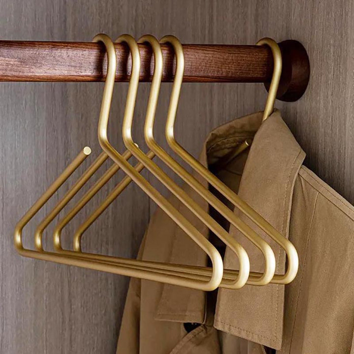 Set of golden aluminium hangers on wooden rod, sleek and durable closet organisers for coats or shirts.