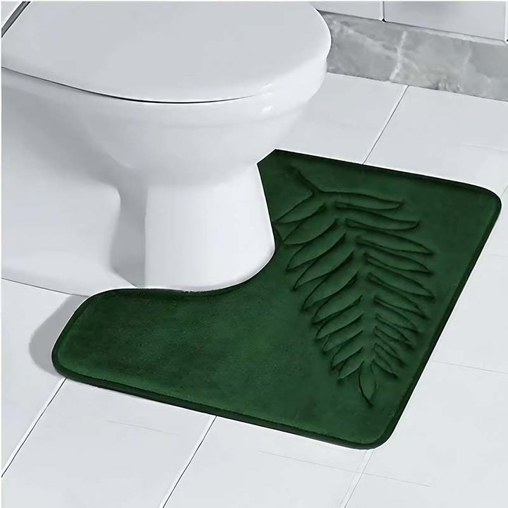 Green bath mat with leaf pattern in front of a white toilet on a tiled bathroom floor.