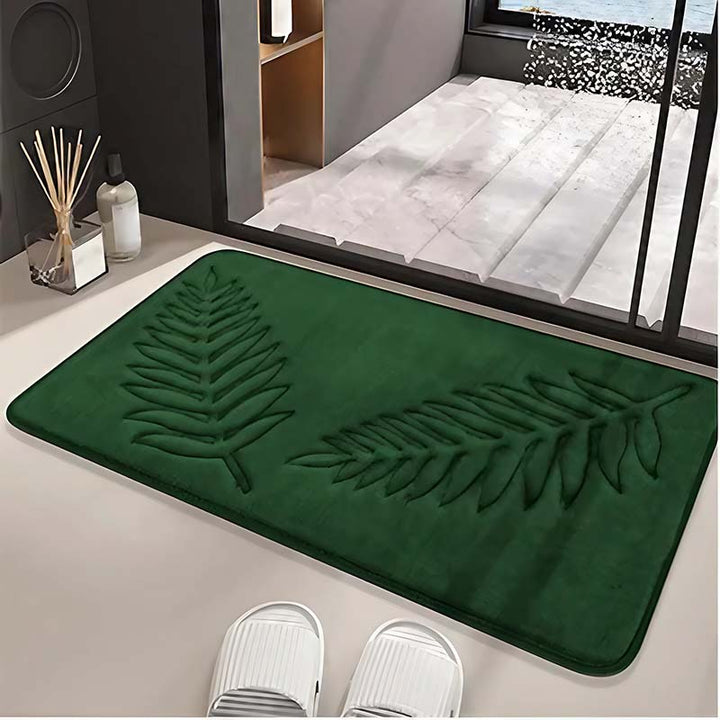 Green bathroom rug with leaf design on a floor, with white sandals and a glass of water nearby.