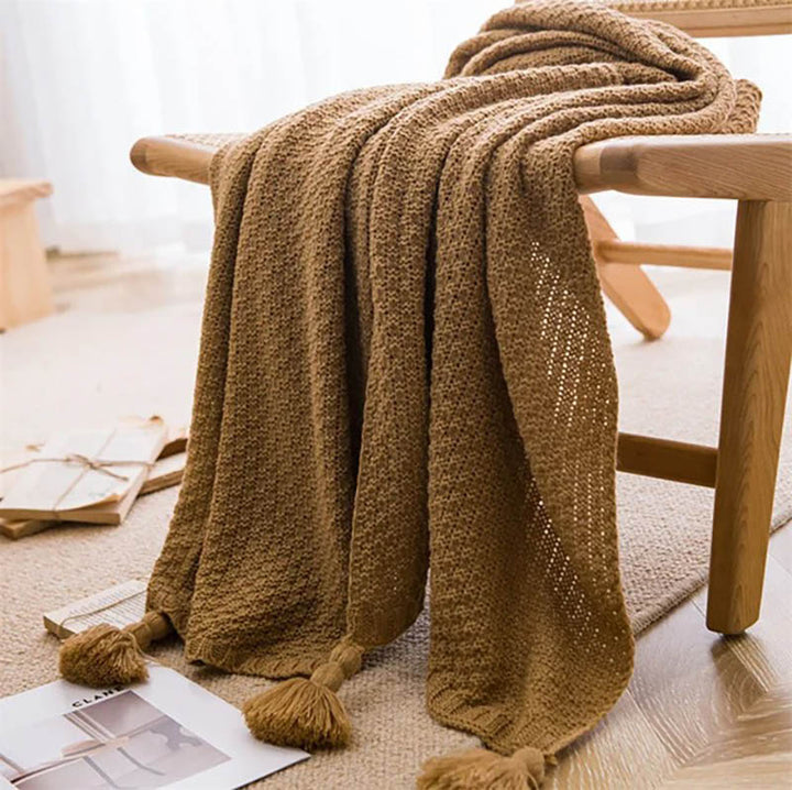Neutral-toned Nordic knitted throw blankets with tassels, soft cotton blend, folded on chair, ideal for sofa or bed. Brown