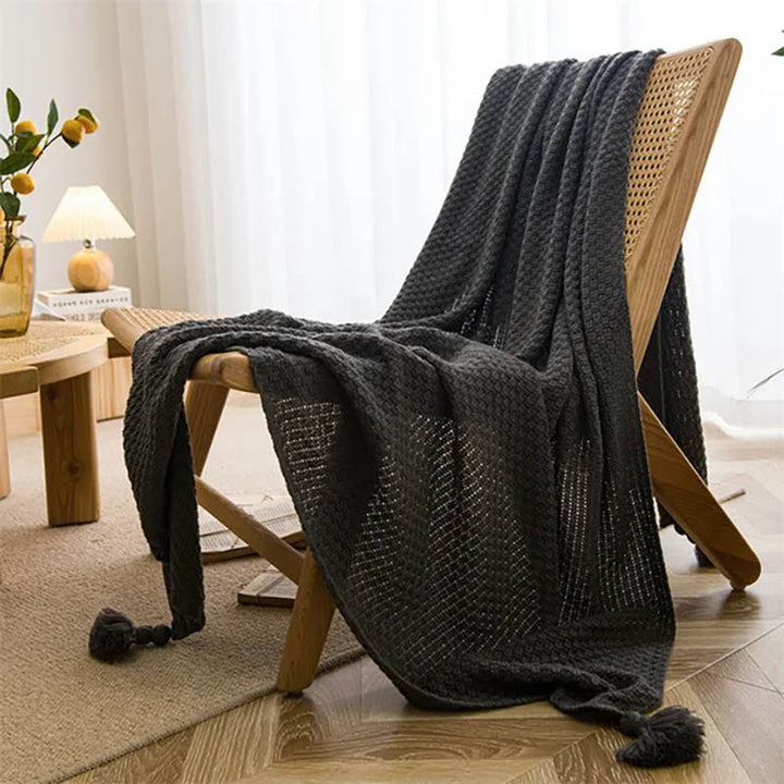Neutral-toned Nordic knitted throw blankets with tassels, soft cotton blend, folded on chair, ideal for sofa or bed. Dark Grey