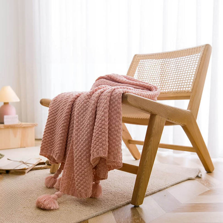 Neutral-toned Nordic knitted throw blankets with tassels, soft cotton blend, folded on chair, ideal for sofa or bed. Pink