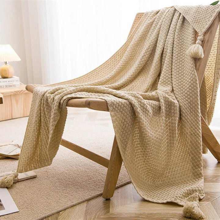 Neutral-toned Nordic knitted throw blankets with tassels, soft cotton blend, folded on chair, ideal for sofa or bed. Khaki