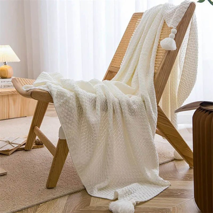 Neutral-toned Nordic knitted throw blankets with tassels, soft cotton blend, folded on chair, ideal for sofa or bed. White