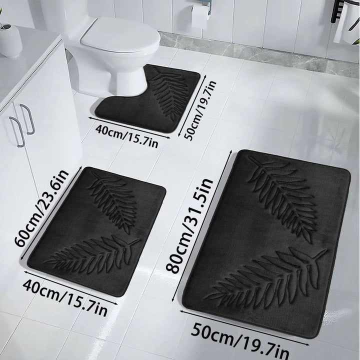 Set of three black bath mats with leaf pattern on a bathroom floor, showing measurements.