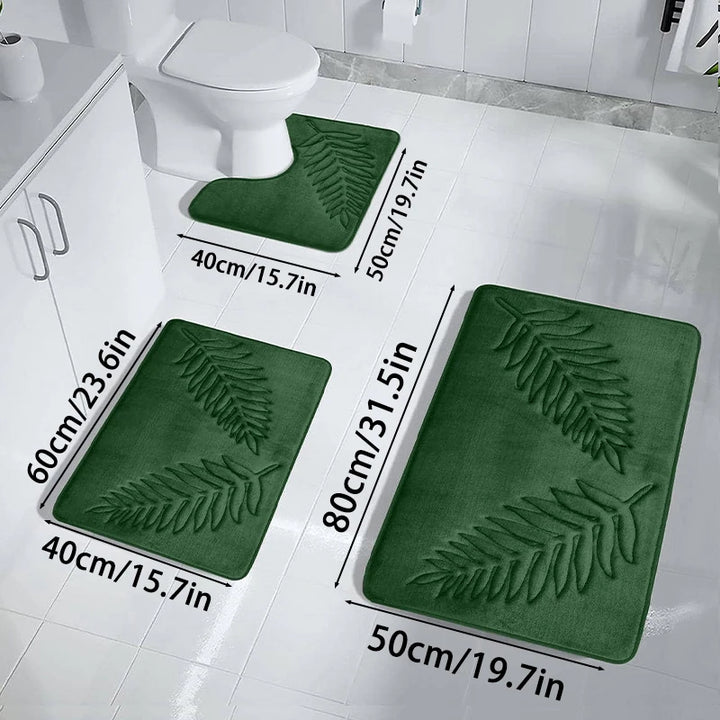 Set of green bath mats with leaf pattern on a white bathroom floor.