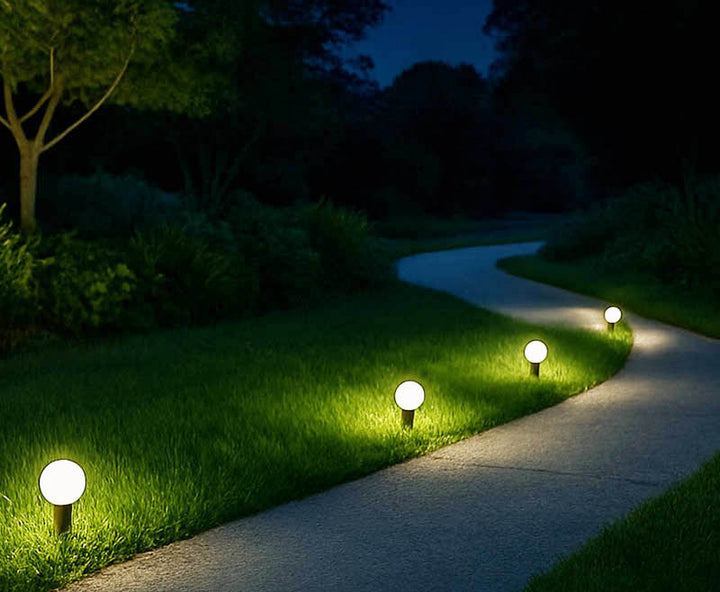 Four small solar-powered globe path lights with warm LED glow lining curved garden path, 4inch / 10cm ABS spheres