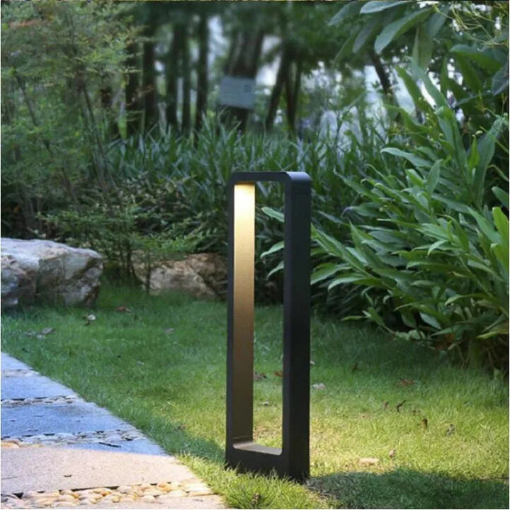 Garden light fixture on a grassy area with plants and rocks in the background