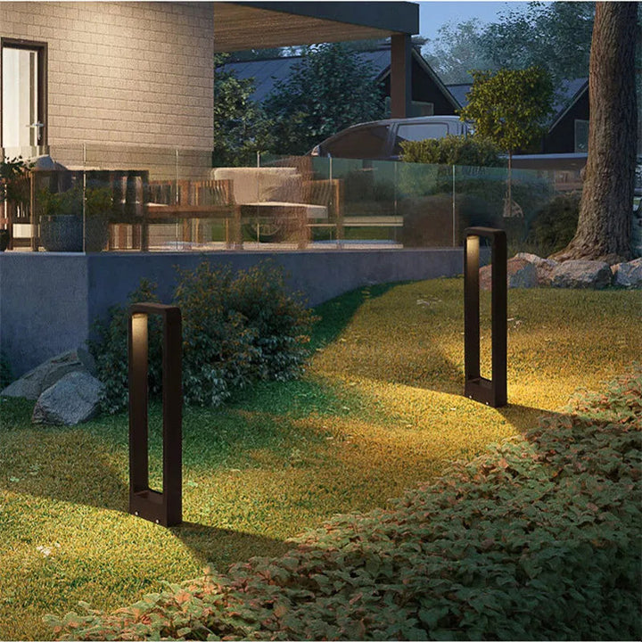 Two outdoor garden lights illuminating a grassy area with a patio and trees in the background.